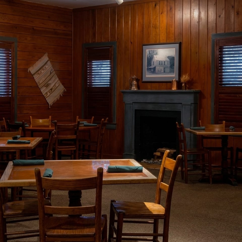 Warm, rustic dining room with wooden tables, chairs, wood-paneled walls, and a central fireplace.