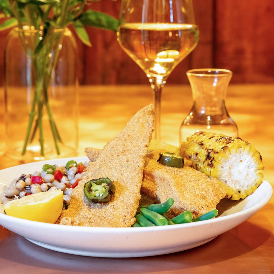 Fried fish with black-eyed peas, green beans, grilled corn, and a lemon wedge, with white wine.