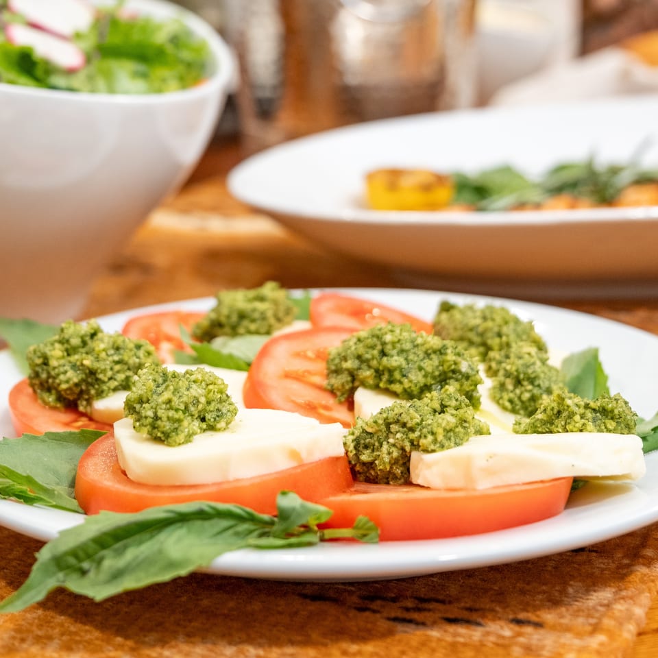 Caprese salad with sliced tomatoes, mozzarella, pesto, and fresh basil on a white plate.